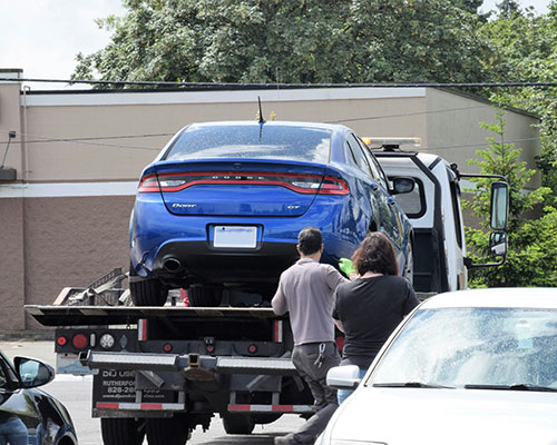 Blue sedan getting towed from a company's vehicle recovery services.