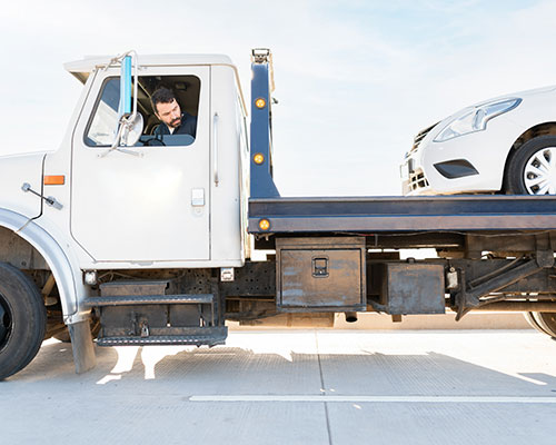 White tow truck with white sedan on the back